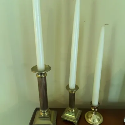 Sale Photo Thumbnail #327: Set of three vintage brass candlesticks in graduated heights, featuring classical reeded columns and square pedestal bases, holding white taper candles.