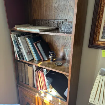 Sale Photo Thumbnail #299: Traditional oak bookcase with bottom cabinet doors, holding various vintage books, glassware, and decorative collectibles.