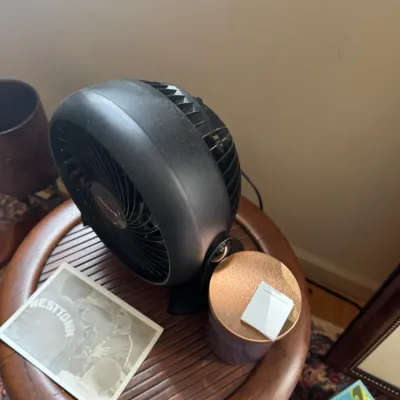 Sale Photo Thumbnail #291: Compact Honeywell black plastic desk fan sitting on a small wooden side table alongside a jar and a vintage Westtown black-and-white photograph.
