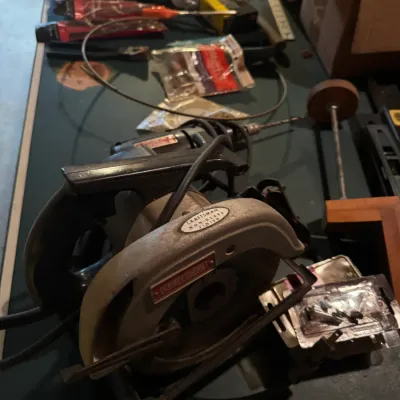 Sale Photo Thumbnail #90: Vintage Craftsman handheld circular saw with non-glare finish, resting on a workbench alongside various hardware and tools.