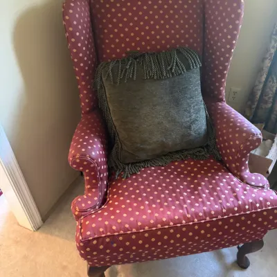 Sale Photo Thumbnail #375: Traditional wingback armchair upholstered in a red and tan polka dot fabric, featuring cabriole wooden legs and a grey fringed accent pillow.