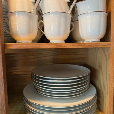 Sale Photo Thumbnail #233: Set of fine white porcelain china featuring silver rim detailing, including stacked teacups, saucers, and plates organized inside a wooden cabinet.