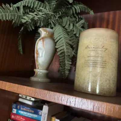 Sale Photo Thumbnail #115: Small onyx marble vase and a Serenity aromatherapy pillar candle displayed on a wooden shelf above a stack of books.