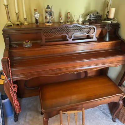 Sale Photo Thumbnail #328: Traditional wooden spinet piano with a matching cabriole-leg bench and decorative lattice music stand, surrounded by various brass candlesticks and collectible figurines.