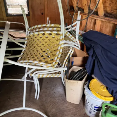 Sale Photo Thumbnail #69: Stack of vintage outdoor patio chairs featuring white metal frames and yellow-and-white woven vinyl strap seating, stored inside a shed.