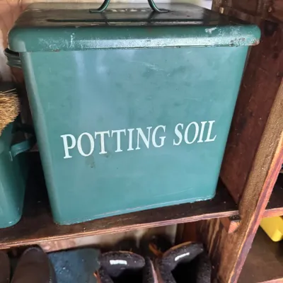 Sale Photo Thumbnail #25: Vintage green metal potting soil container with a fitted lid and top handle, resting on a wooden shelf.