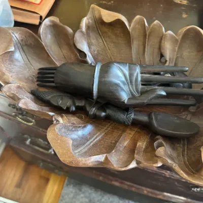 Sale Photo Thumbnail #120: Vintage carved wooden leaf-shaped bowl filled with dark hand-carved wooden server utensils, including hand-shaped serving forks and figure-detailed spoons.