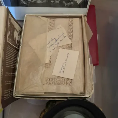 Sale Photo Thumbnail #338: Vintage box containing a embroidered lace linen placemat set with handwritten note and calling card, displayed alongside books and a small music box.