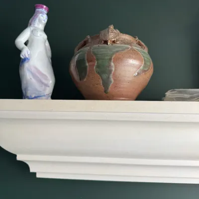 Sale Photo Thumbnail #275: Decorative ceramic items displayed on a white floating shelf, including a glazed studio art pottery vase with a turtle embellishment and a hand-painted porcelain female figurine.