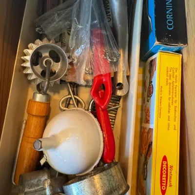 Sale Photo Thumbnail #229: Kitchen drawer filled with vintage gadgets, including a wooden-handled pastry wheel, enamelled funnel, aluminum metal cutters, and boxed Westmark Decoretto garnishing tools.