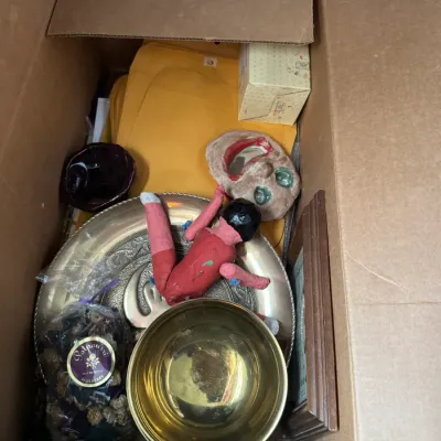 Sale Photo Thumbnail #133: Cardboard box filled with assorted household goods, including brass bowls, decorative masks, a bag of potpourri, and manila envelopes.
