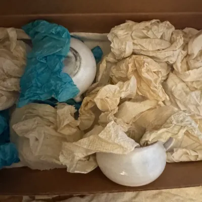 Sale Photo Thumbnail #348: Collection of white ceramic tea cups and pottery packed in tissue paper inside a cardboard box.