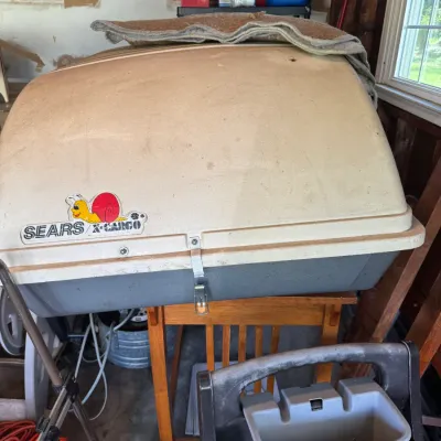 Sale Photo Thumbnail #200: Vintage Sears X-Cargo rooftop carrier with original snail logo decal, sitting in a garage setting.