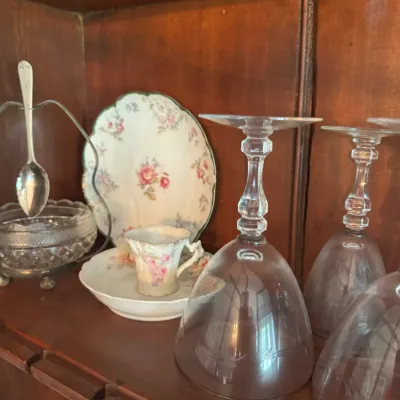Sale Photo Thumbnail #399: Collection of vintage glassware and china inside a wooden hutch, featuring inverted crystal stemware, floral china tea pieces, and a silver-plated spoon holder with a cut glass bowl.