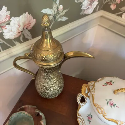 Sale Photo Thumbnail #387: Vintage ornamental brass Middle Eastern dallah coffee pot featuring detailed embossed floral patterns, displayed alongside a floral porcelain tureen.