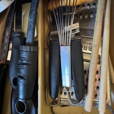 Sale Photo Thumbnail #254: Assorted vintage kitchen utensils organized in a drawer, including wire whisks, wooden spoons, a metal grater, and knives.