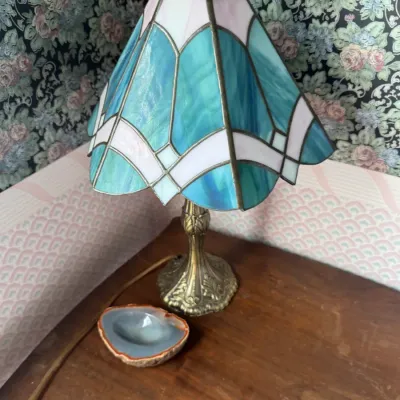 Sale Photo Thumbnail #132: Small Tiffany-style stained glass table lamp featuring a blue and white geometric shade on an ornate brass-toned base, shown alongside a polished agate slice dish.