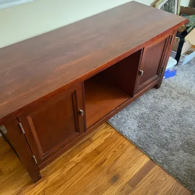 Sale Photo Thumbnail #122: Warm cherry-toned wooden media console featuring a central open compartment and two side cabinet doors with silver-toned hardware.
