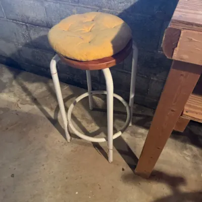 Sale Photo Thumbnail #77: Vintage white metal bar stool with a wood-tone seat topped by a tufted yellow cushion.