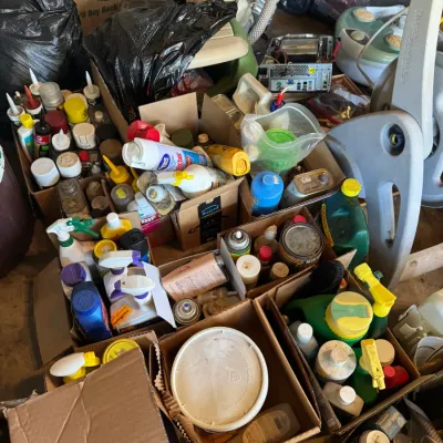 Sale Photo Thumbnail #206: Assorted household chemical supplies, spray bottles, and paints packed in cardboard boxes, alongside lawn care items and miscellaneous garage gear.
