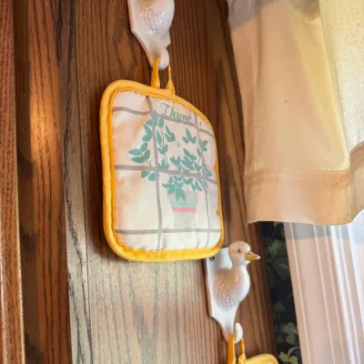 Sale Photo Thumbnail #264: Pair of vintage duck-shaped ceramic wall hooks holding matching herb-patterned cloth pot holders.