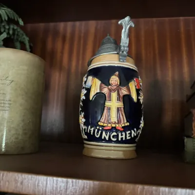 Sale Photo Thumbnail #116: German lidded beer stein featuring a raised relief design of the Münchner Kindl and 'MÜNCHEN' lettering, with a pewter lid.