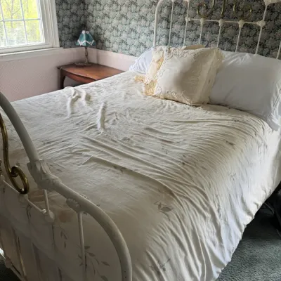 Sale Photo Thumbnail #137: Vintage white wrought iron and brass bed frame featuring scrollwork accents, set with cream bedding.