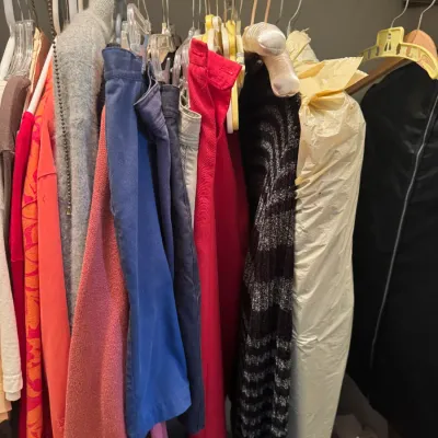 Sale Photo Thumbnail #102: Closet rod filled with assorted vintage and modern women's clothing on hangers, including sweaters, pants, and dry-cleaned garments.