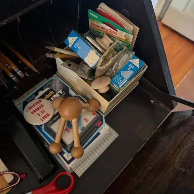 Sale Photo Thumbnail #182: Assorted desk supplies and novelties organized inside a dark wood secretary desk compartment, including Scotch mounting strips, pencils, scissors, and a wooden puzzle toy.