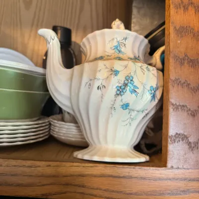 Sale Photo Thumbnail #270: Vintage fluted ceramic teapot with a blue floral pattern, shown stored in a wooden cabinet.