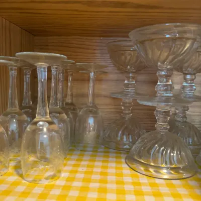 Sale Photo Thumbnail #242: Collection of clear glassware inside a wooden cabinet, including etched wine glasses stored upside down and stackable pressed glass coupes with swirl patterns.