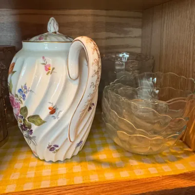 Sale Photo Thumbnail #244: Vintage white porcelain teapot with a spiral swirl design, floral motif, and gold filigree accents, displayed next to stacked clear glass scalloped bowls.