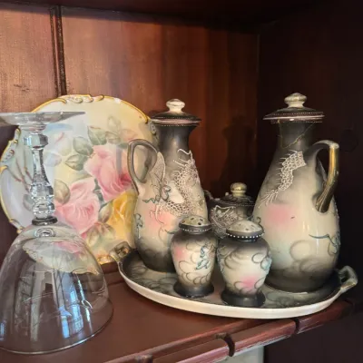 Sale Photo Thumbnail #395: Vintage Japanese dragonware porcelain sake or condiment set with matching tray, salt and pepper shakers, and lidded cruets, displayed alongside hand-painted floral porcelain plates.