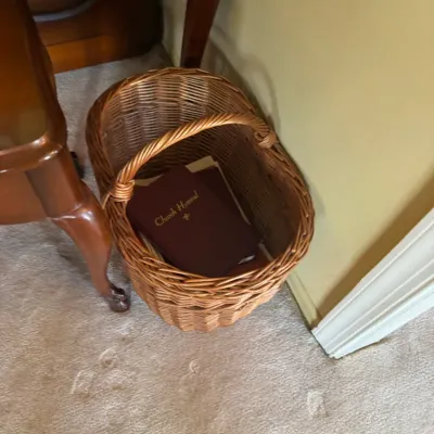 Sale Photo Thumbnail #320: Woven wicker gathering basket with a fixed handle containing a burgundy Church Hymnal and other books.