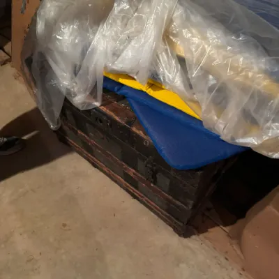 Sale Photo Thumbnail #83: Antique wooden steamer trunk with metal hardware and wood slats, partially covered by plastic sheeting and mats.