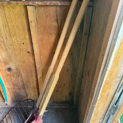 Sale Photo Thumbnail #67: Heavy-duty post hole digger with long wooden handles and red steel blades, leaning inside a wooden shed.