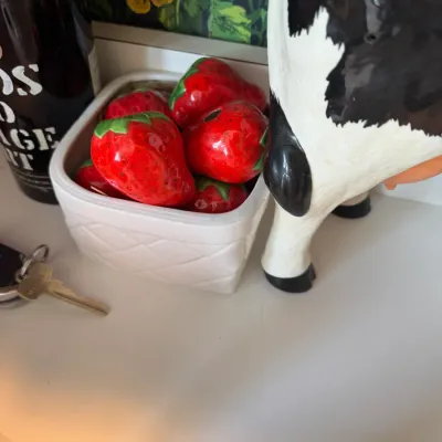 Sale Photo Thumbnail #247: Vintage ceramic strawberry cluster in a white basket planter alongside a black-and-white ceramic cow creamer.
