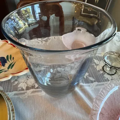 Sale Photo Thumbnail #417: Large clear glass punch bowl with a wide flared rim, set on a lace tablecloth among other glassware.