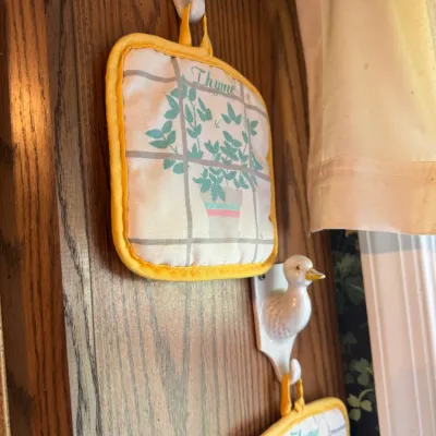 Sale Photo Thumbnail #265: Vintage fabric potholders featuring a potted thyme graphic and yellow trim, hanging from duck-shaped ceramic wall hooks.