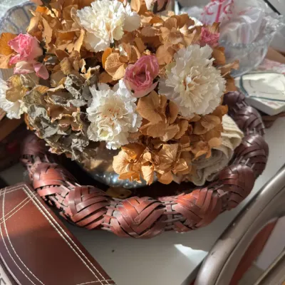 Sale Photo Thumbnail #218: Dried floral arrangement featuring pink roses, white carnations, and hydrangeas, resting inside a dark reddish-brown woven basket tray.