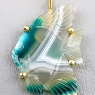 Sale Photo Thumbnail #12: Carved gemstone fish pendant featuring banded agate with teal and white hues, set with yellow gold accents and a gold bail.