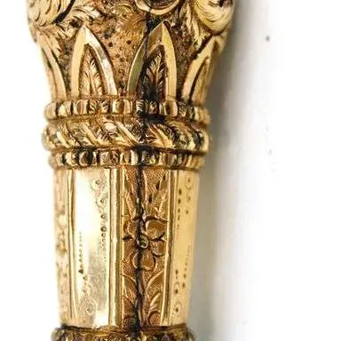 Sale Photo Thumbnail #22: Antique walking cane featuring an ornately carved, gold-toned handle with intricate floral scrollwork and detailed band accents.