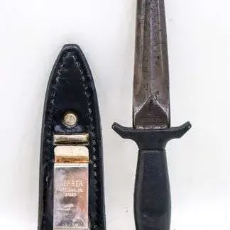 Sale Photo Thumbnail #16: Vintage Gerber Guardian boot knife with double-edged blade and textured black handle, paired with its original black leather sheath featuring a metal boot clip.