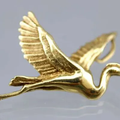 Sale Photo Thumbnail #6: Gold-tone pendant or brooch crafted in the shape of a crane in flight, featuring detailed feather texture on the wings.