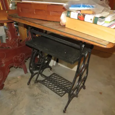 Sale Photo Thumbnail #60: Vintage treadle sewing machine table base repurposed with a wooden tabletop, clutter, and an ornate carved wooden headboard nearby.
