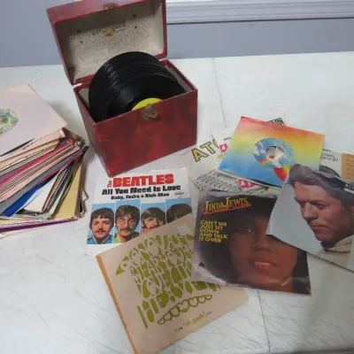 Sale Photo Thumbnail #131: Collection of vintage 45 RPM vinyl records and picture sleeves, including a red textured storage case and artists like The Beatles, Linda Lewis, and Donovan.
