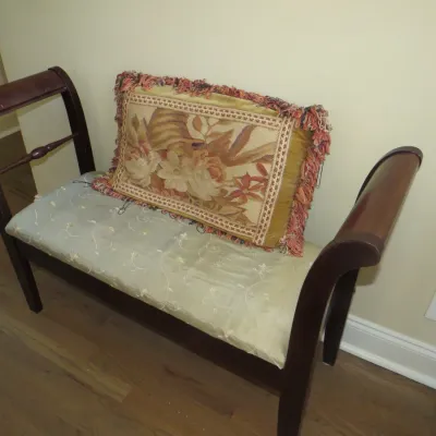 Sale Photo Thumbnail #20: Traditional dark wood accent bench with an upholstered seat, rolled armrests, and an included fringed floral tapestry accent pillow.