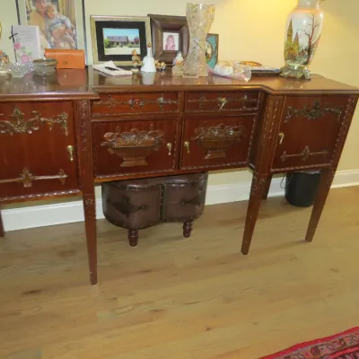 Sale Photo Thumbnail #33: Antique carved mahogany sideboard featuring ornamental relief panels and brass hardware, topped with various decor items including picture frames and glassware.