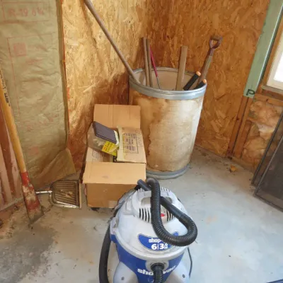 Sale Photo Thumbnail #53: A blue and grey Shop-Vac wet/dry vacuum with hose, displayed alongside cardboard boxes and a metal bin holding various long-handled garden tools.