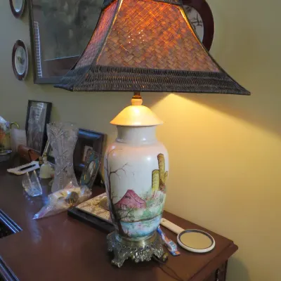 Sale Photo Thumbnail #31: Hand-painted ceramic urn table lamp featuring a rural barn landscape scene on an ornate brass base, paired with a pyramid-shaped woven wicker lampshade.